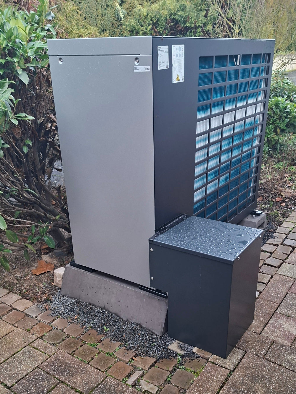 Anthrazitfarbene Bodenabdeckhaube für Wärmepumpe, montiert an Buderus Wärmepumpe im Garten, nachhaltige Schutzabdeckung aus Metall“